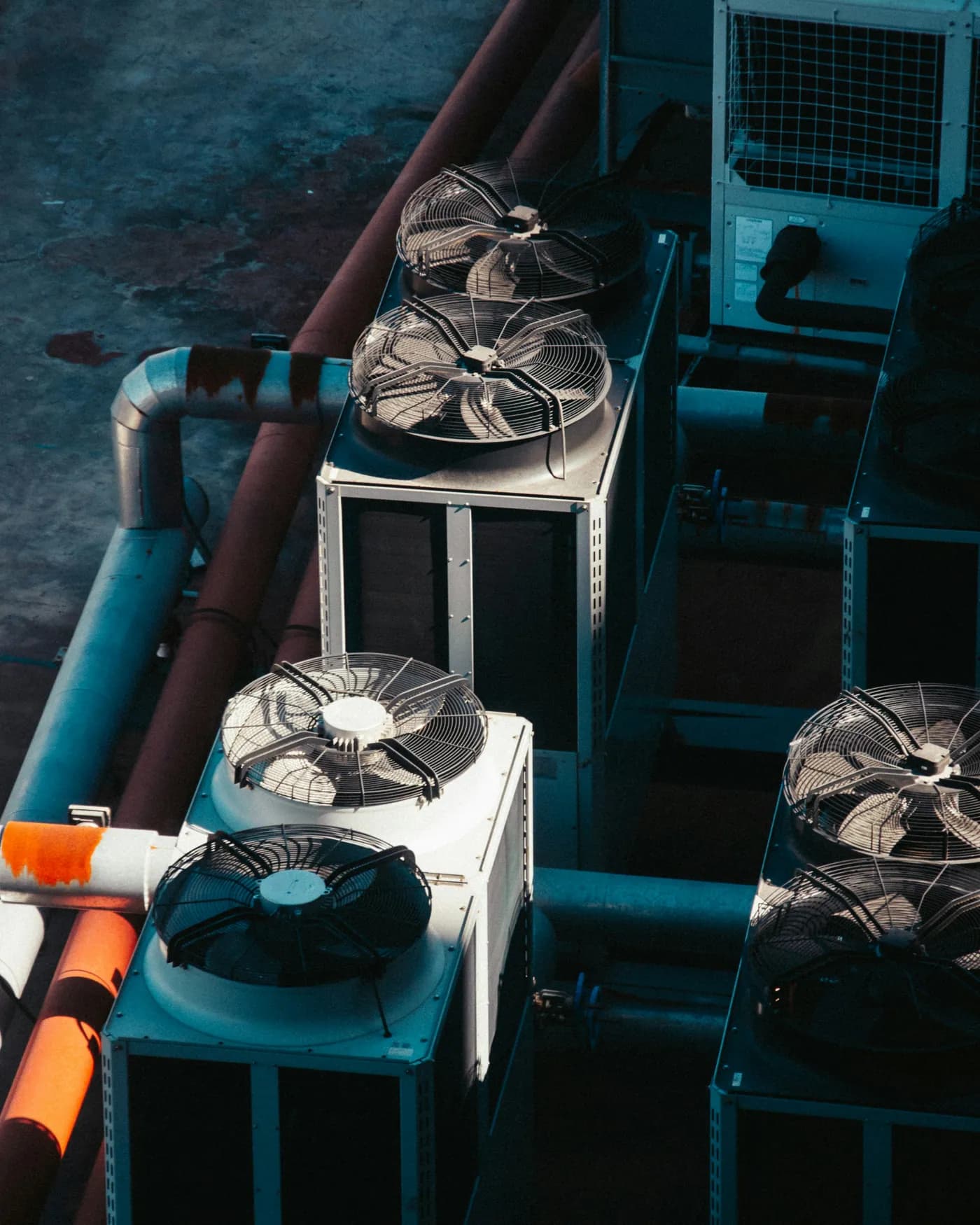 Rooftop condenser units with large fans, seen from above beside insulated refrigerant pipework